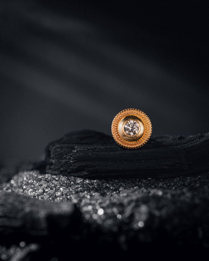 Gold earring with intricate design on a dark textured surface