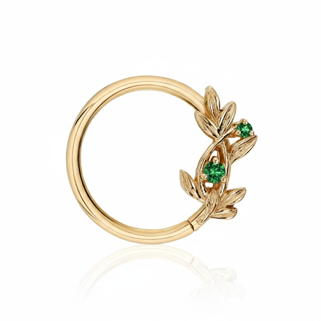 Gold ring with leaf design and green gemstones on a white background